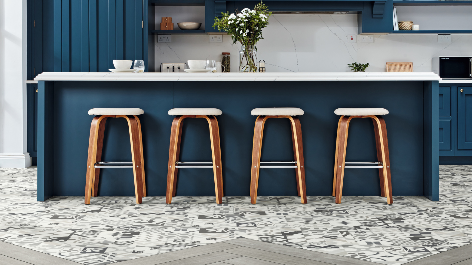 The use of non-uniform patchwork arrangement white and black flooring and a clean gray wash timber look (Grano WP311) in a herringbone pattern separates the kitchen from other areas